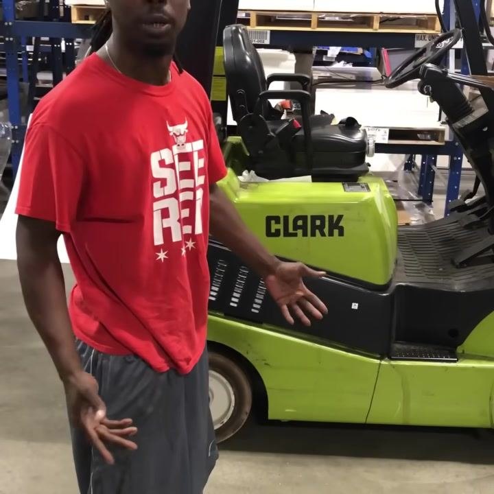 Operator standing beside the green CLARK forklift, gesturing with hands while explaining. Warehouse environment visible.