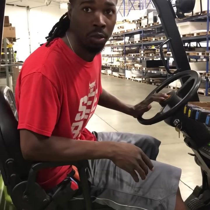 Forklift operator's seat, steering wheel, and visible seatbelt. Operator's hand reaching for controls.