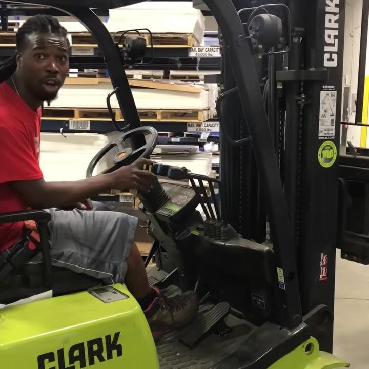 Operator demonstrating tilt lever, hand on second hydraulic control, forklift mast and dashboard visible.