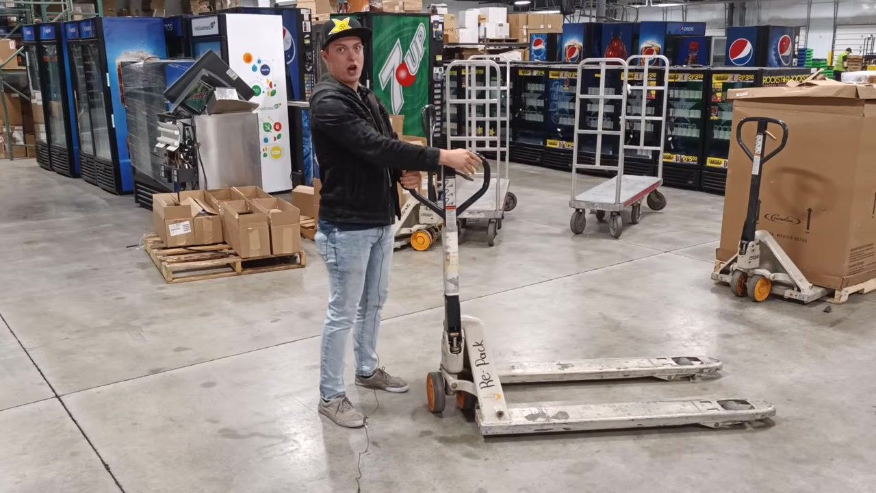 Close-up of a person in a warehouse, pointing and emphasizing safety. A sign reads: "Always remember to think of your coworkers safety and practice good habits!"