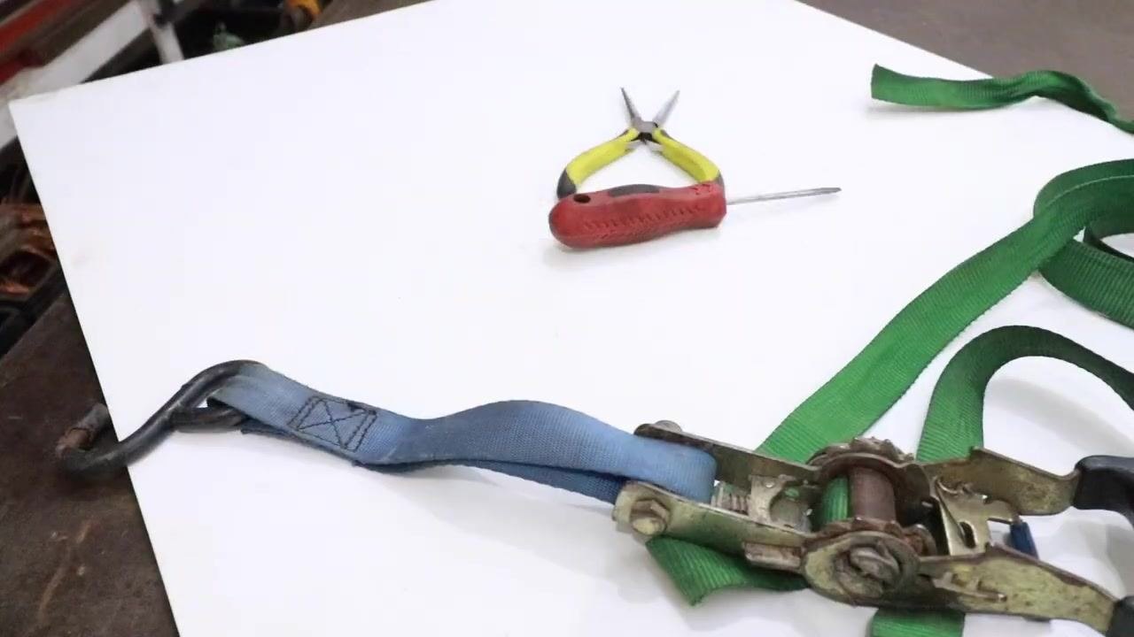 Ratchet strap and green webbing fully released and laid out on the table, with tools set aside.