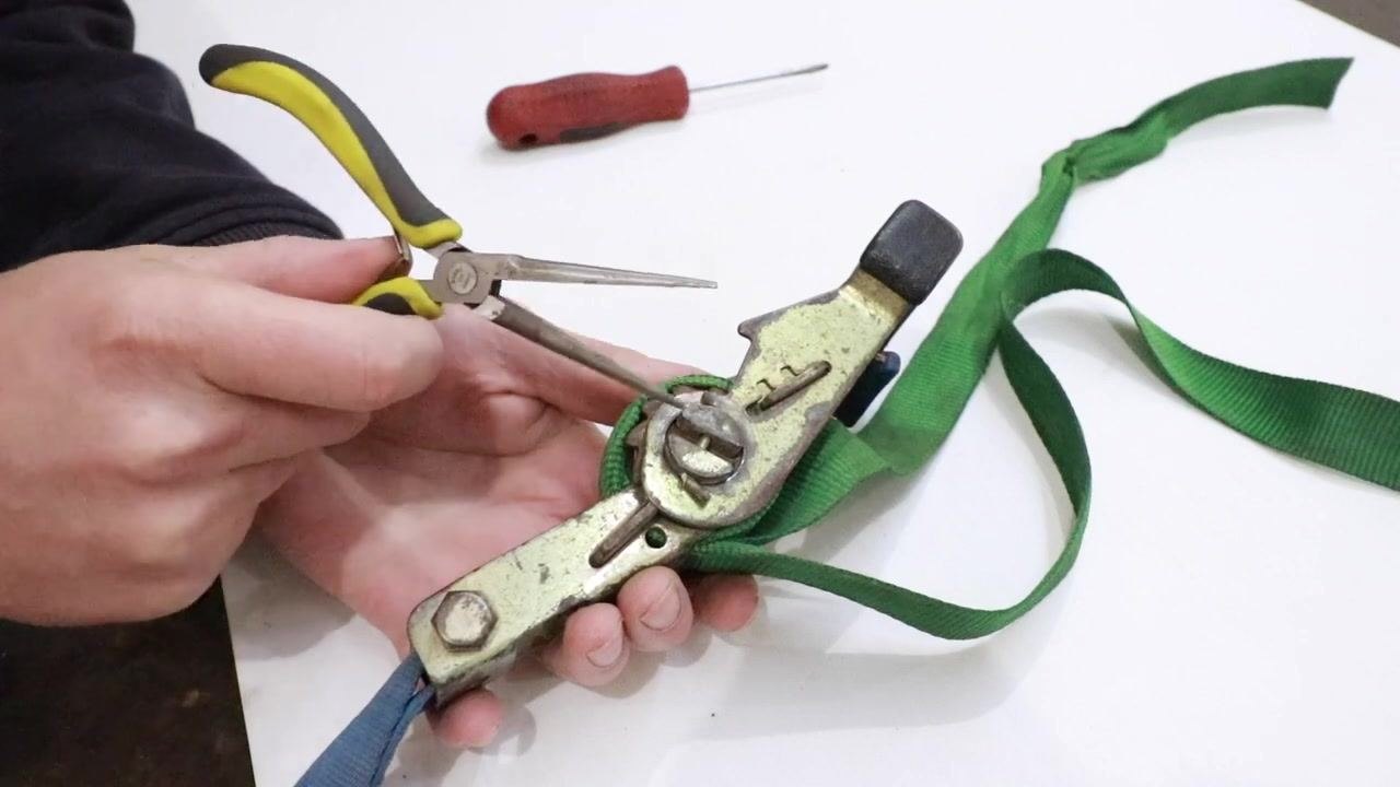 Needle nose pliers positioned to insert into the slot on the ratchet spool.