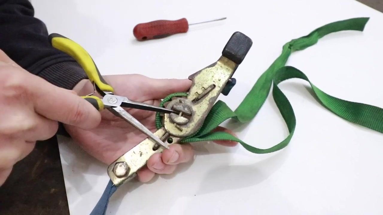 Pliers turning the spool while the webbing is pulled to remove slack.