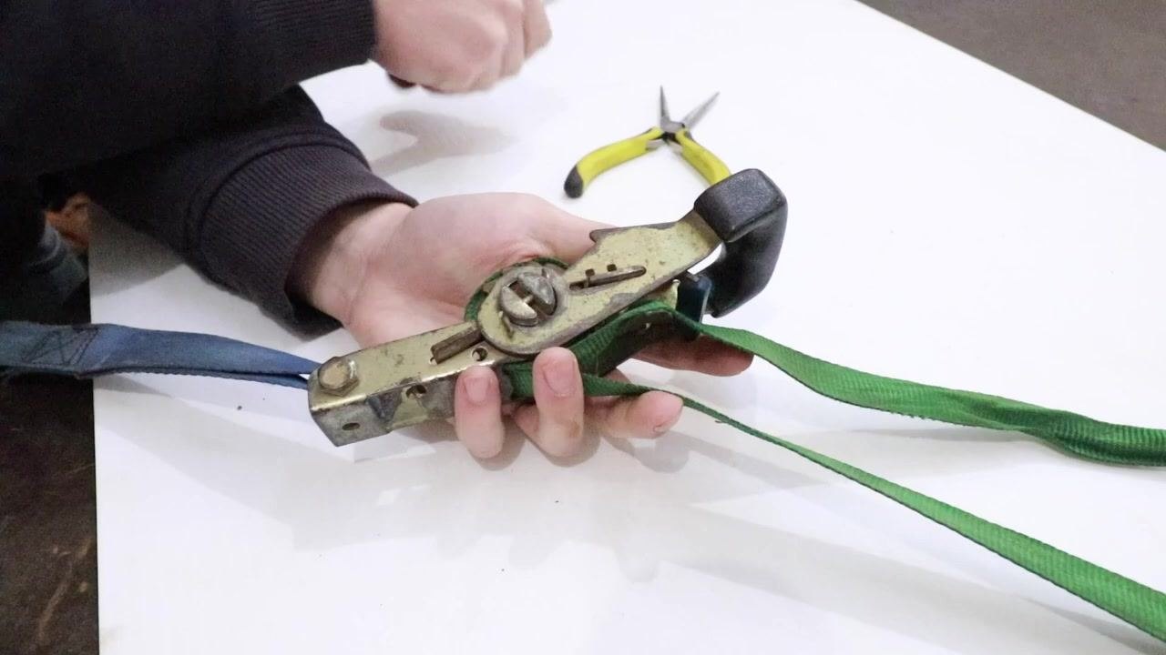 Hand cranking the ratchet strap to intentionally create a tight jam, with tools on the table.