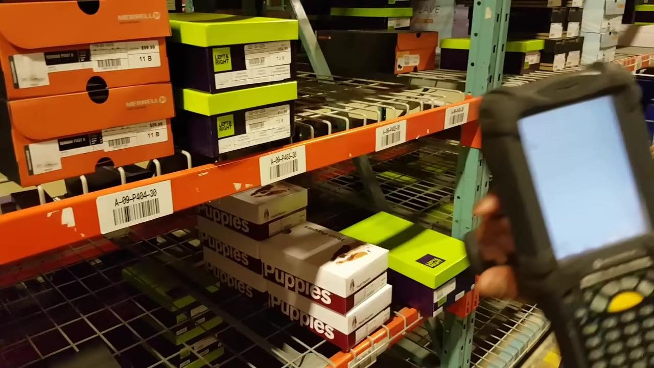 Handheld scanner in the foreground, focused on a shelf with "LEFT & RIGHT" and "Puppies" shoe boxes. Shelf label "A-09-P424-30" is visible.