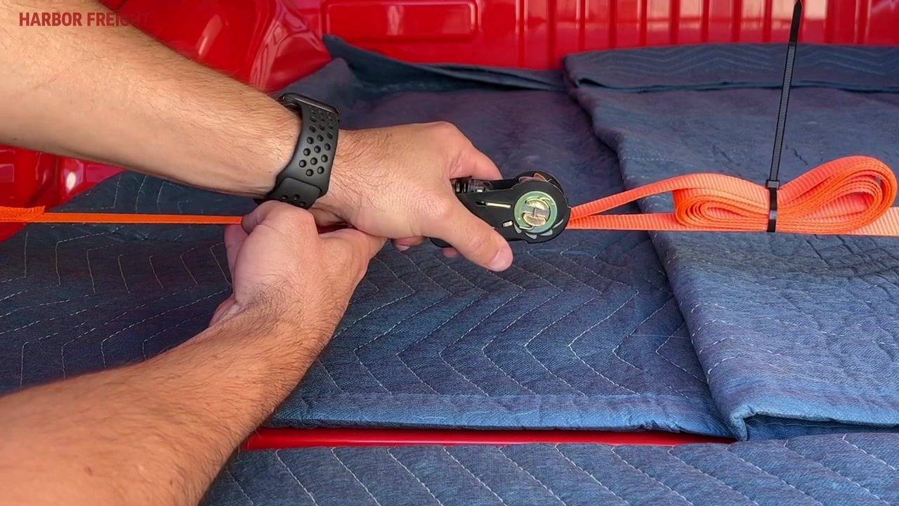 A close-up of hands operating the ratchet release mechanism, with the bundled and zip-tied webbing visible.
