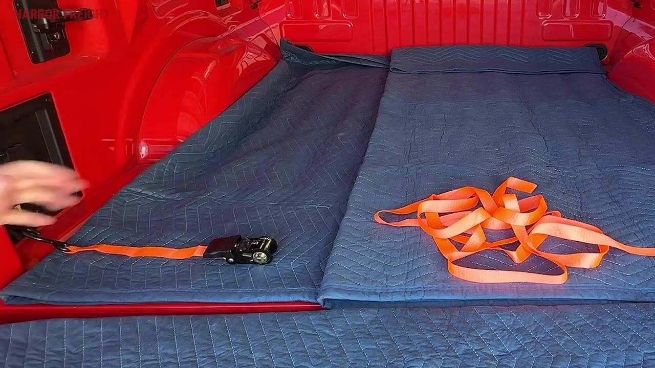 A hand holding and pulling the orange strap between thumb and pointer finger to untangle the webbing in the truck bed.