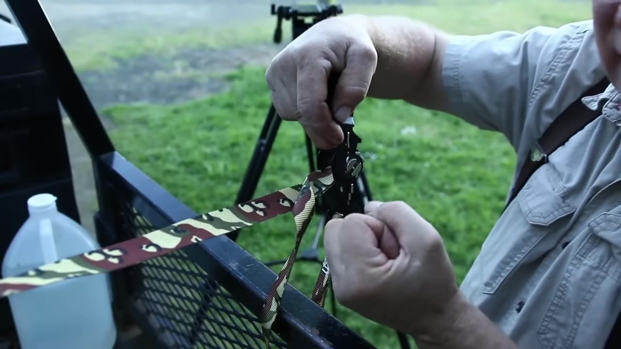 A person pulls the ratchet handle straight, demonstrating release of strap tension as the strap visibly loosens.